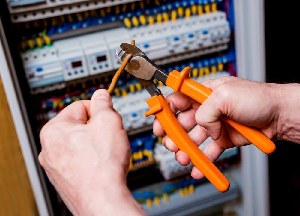 Hands Using Orange Pliers to Cut a Wire in a Control Panel — Darwin Electrical Services in Rural & Remote, NT