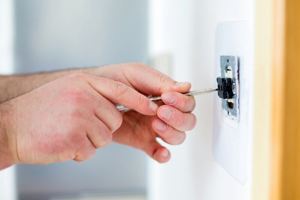 Hands Using a Screwdriver to Install or Repair a Light Switch on a White Wall — Darwin Electrical Services in Humpty Doo, NT