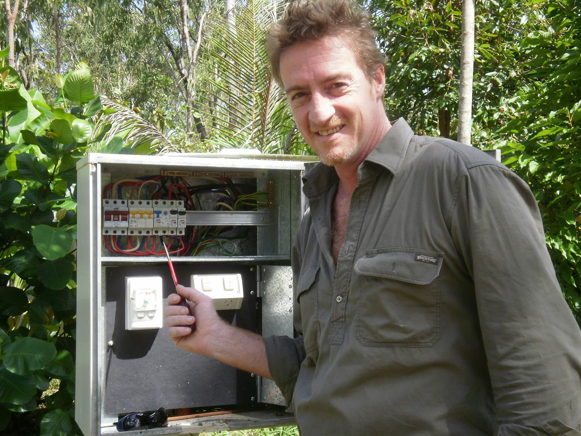 Man beside an open electrical control box, pointing at wiring and switches. — Darwin Electrical Services in Humpty Doo, NT