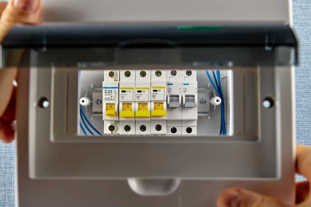 Person Holding an Open Electrical Breaker Box With Yellow and White Switches — Darwin Electrical Services in Humpty Doo, NT