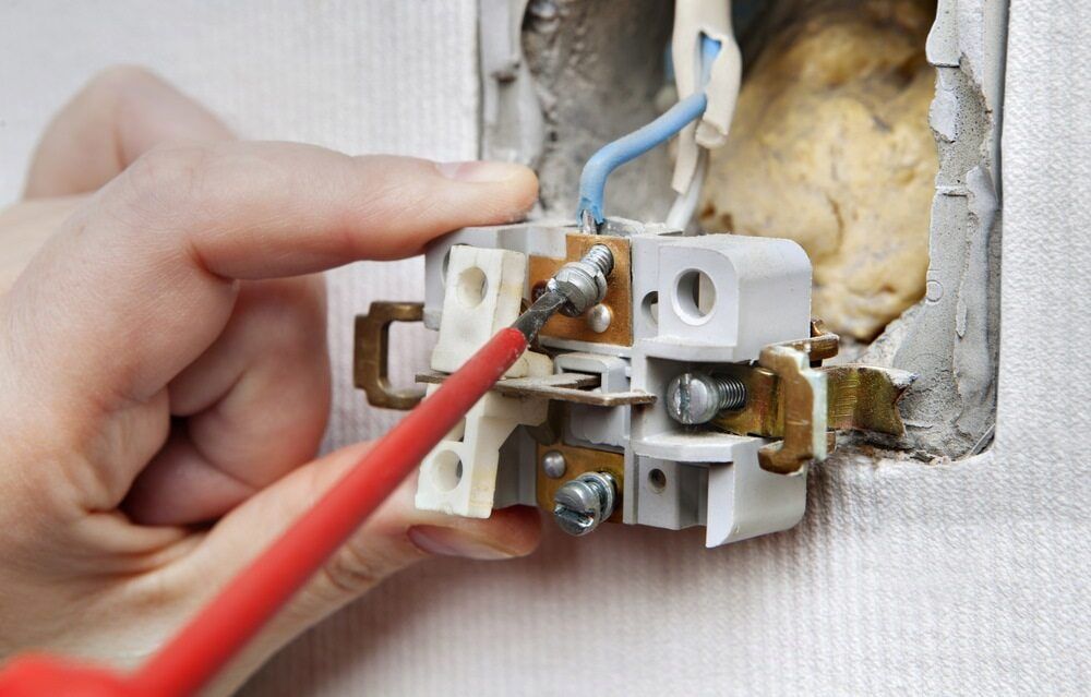 Hand Using a Screwdriver to Wire a Light Switch in a Damaged Wall — Darwin Electrical Services in Humpty Doo, NT
