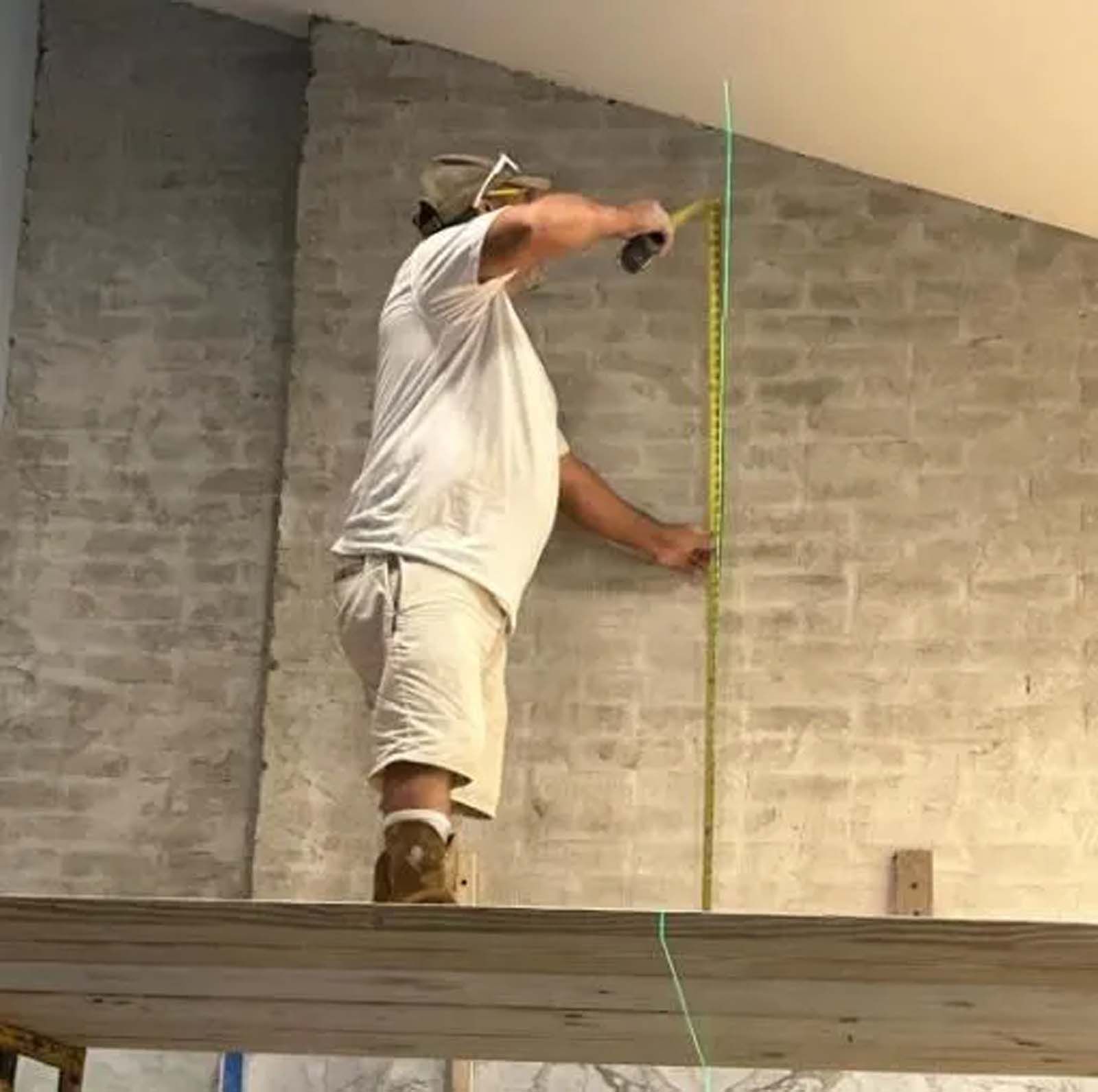 A man is measuring a brick wall with a tape measure.