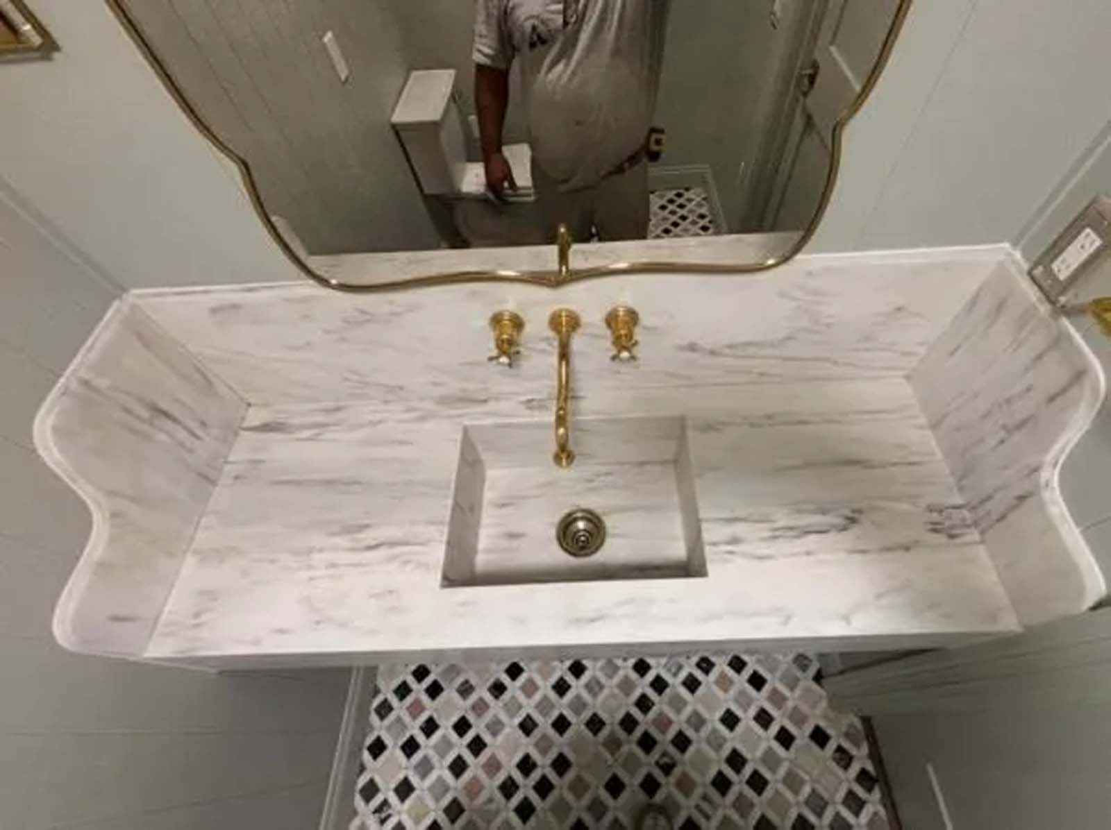 A bathroom sink with a gold faucet and a mirror.