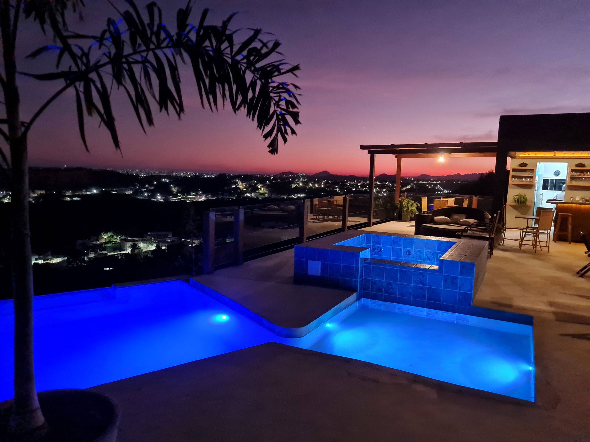 Uma grande piscina é iluminada à noite com vista para a cidade.