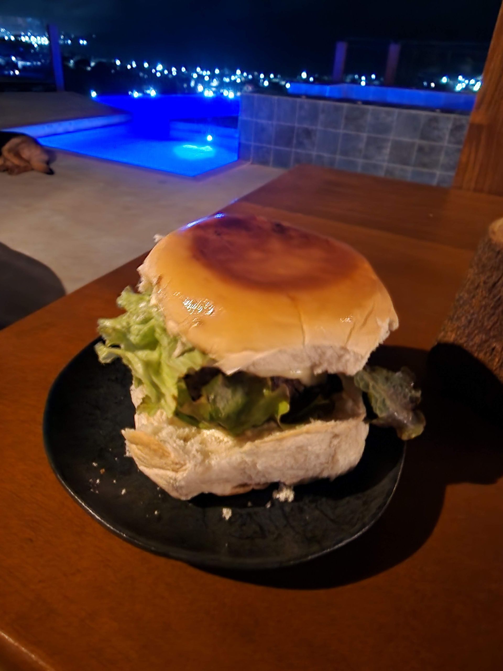 Um hambúrguer está em um prato preto sobre uma mesa de madeira.