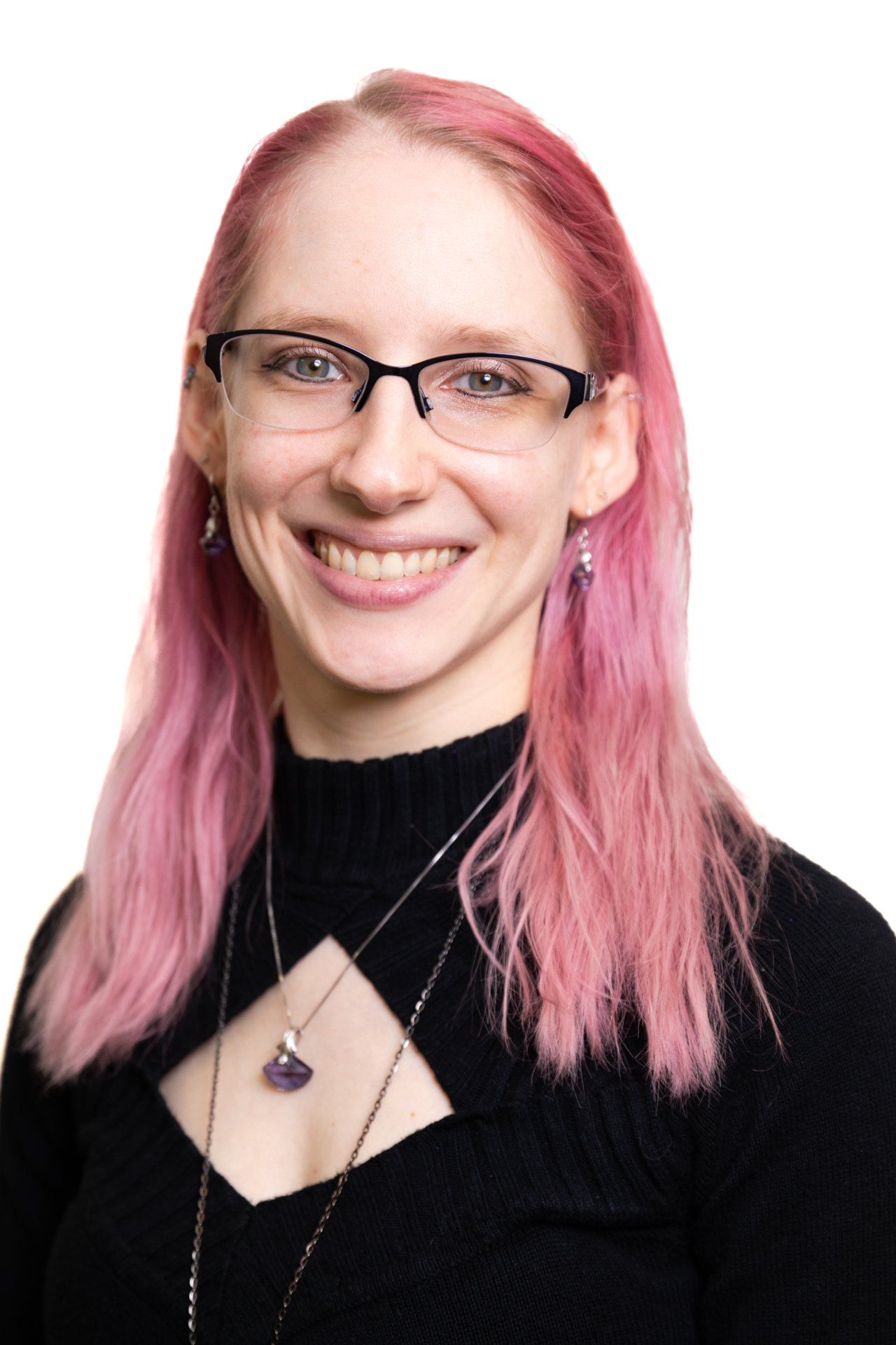 A woman with pink hair and glasses is smiling for the camera.