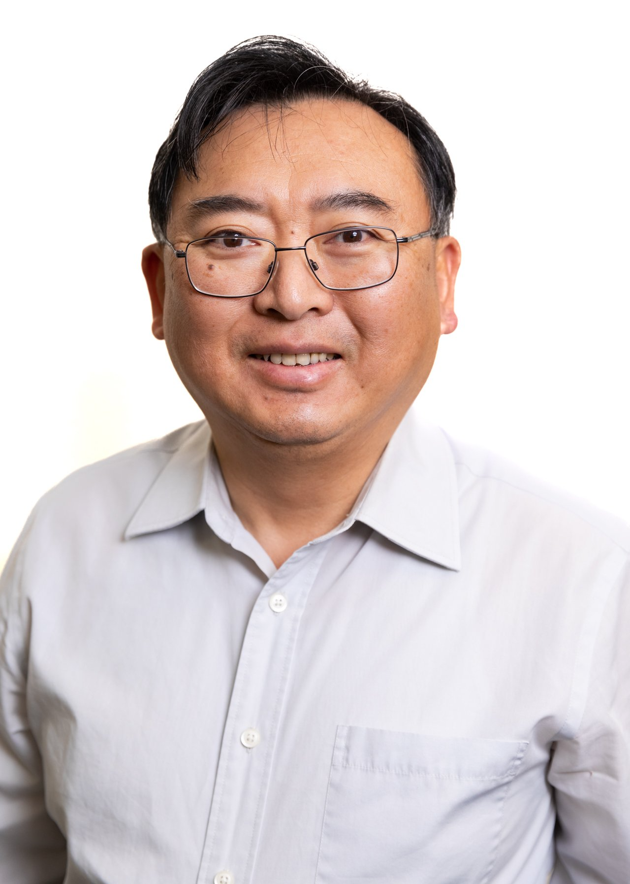A man wearing glasses and a white shirt is smiling for the camera.
