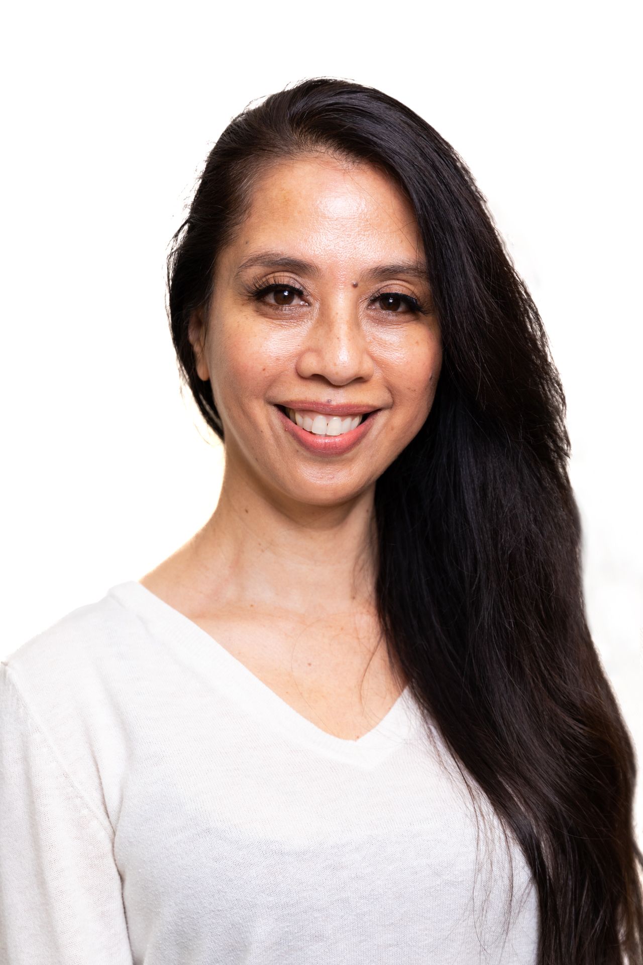 A woman with long black hair is wearing a white shirt and smiling.