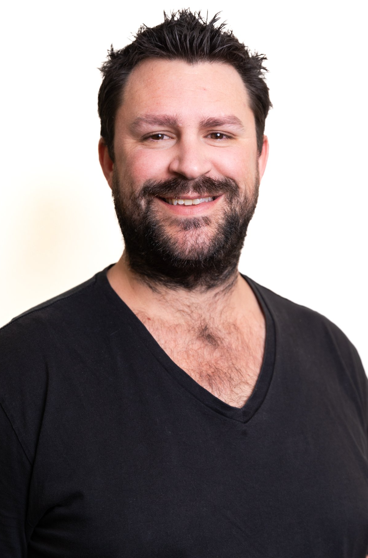 A man with a beard is wearing a black shirt and smiling