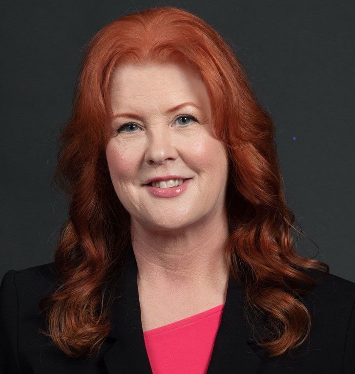 A woman with red hair is wearing a black jacket and a pink shirt.