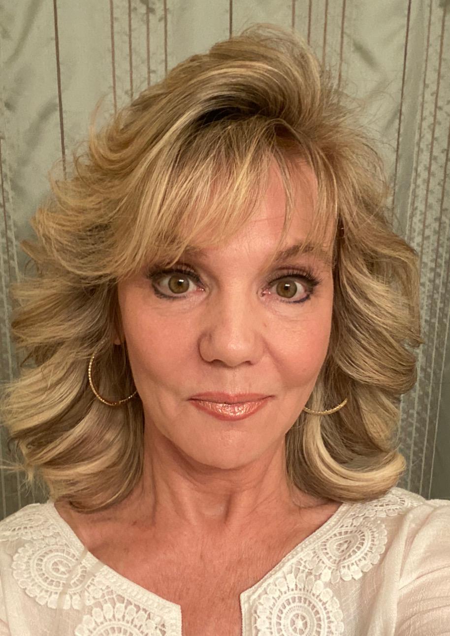 A woman with blonde hair and a white shirt is taking a selfie.
