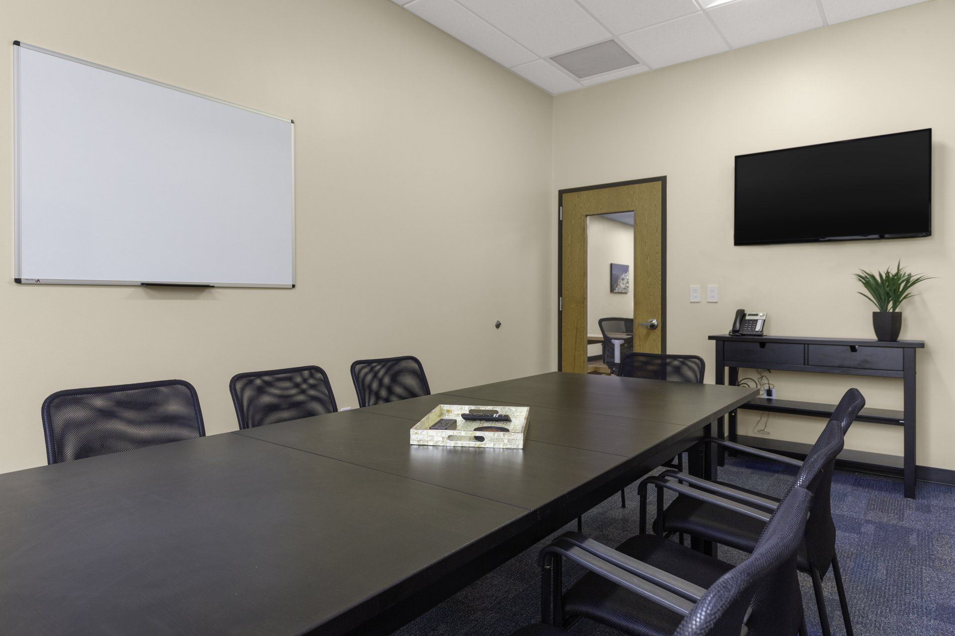 A conference room with a long table , chairs , a whiteboard and a flat screen tv.