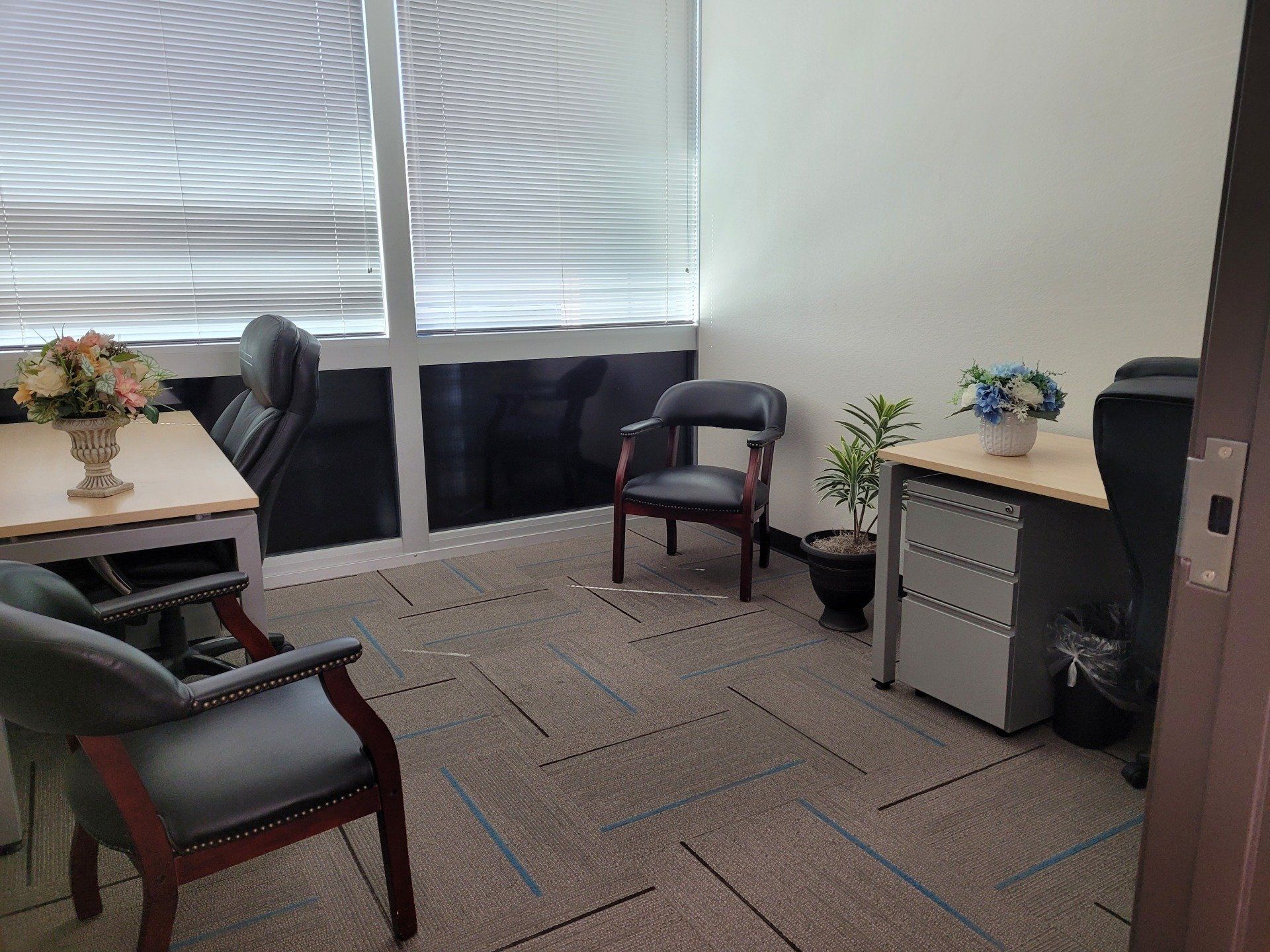 A small office with a desk , chairs , and a plant.
