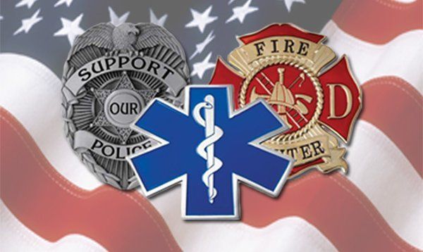 A police badge a fire badge and an ambulance badge are on an american flag
