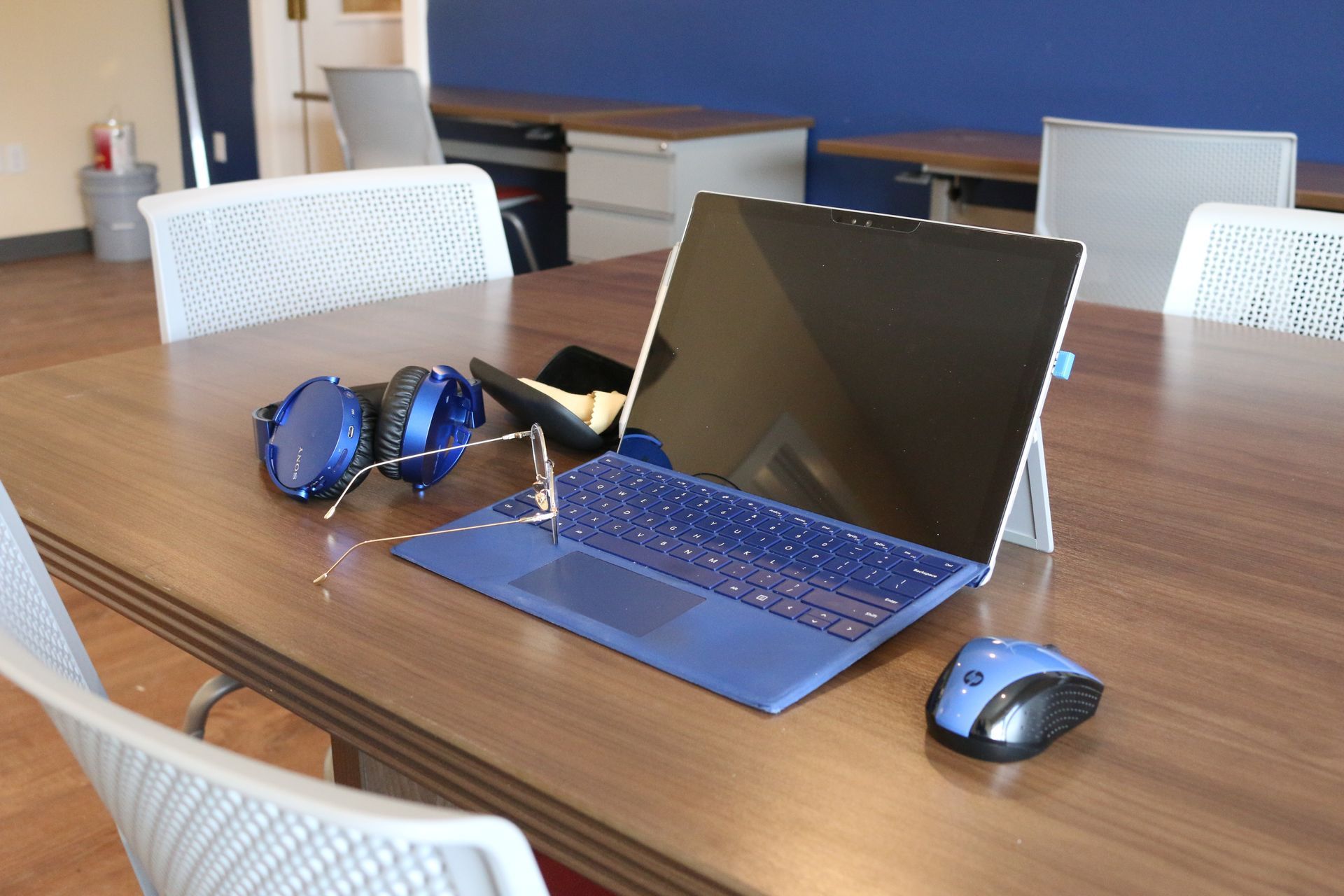 A blue laptop is sitting on a wooden table next to a mouse and headphones.