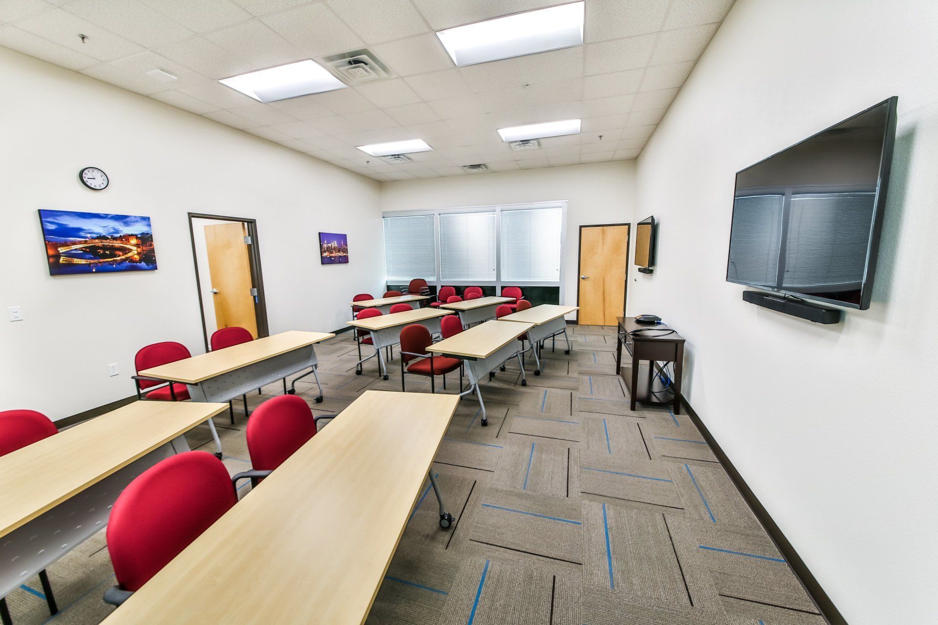 A classroom with tables and chairs and a flat screen tv on the wall.
