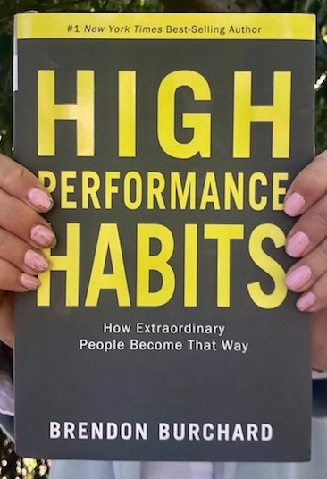 A person is holding a book titled high performance habits