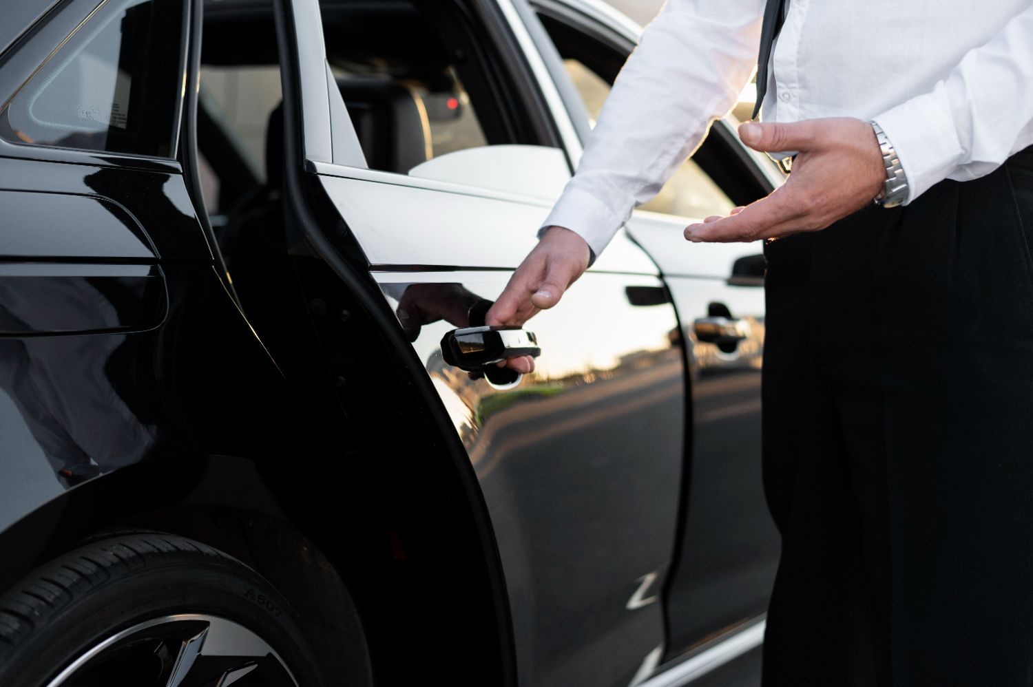 A man in a white shirt and tie is opening the door of a black car.