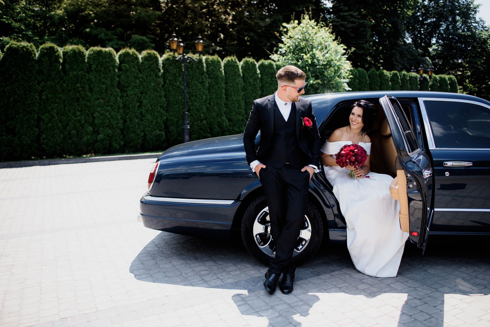 A bride and groom are standing next to a black limousine.