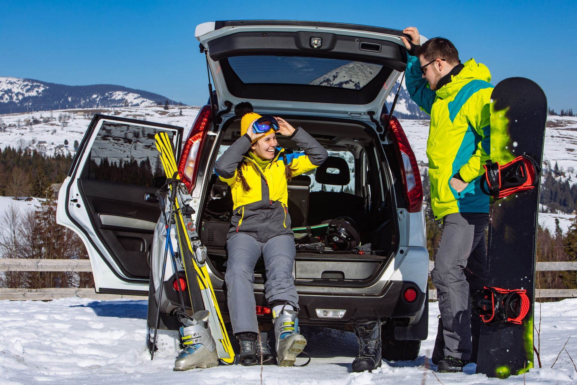 A man and a boy are standing next to a car with skis and snowboards in the back.
