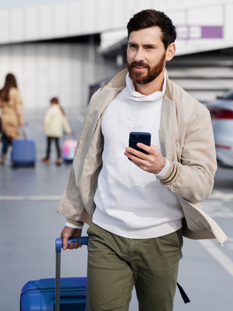 A man is walking with a suitcase and looking at his phone.