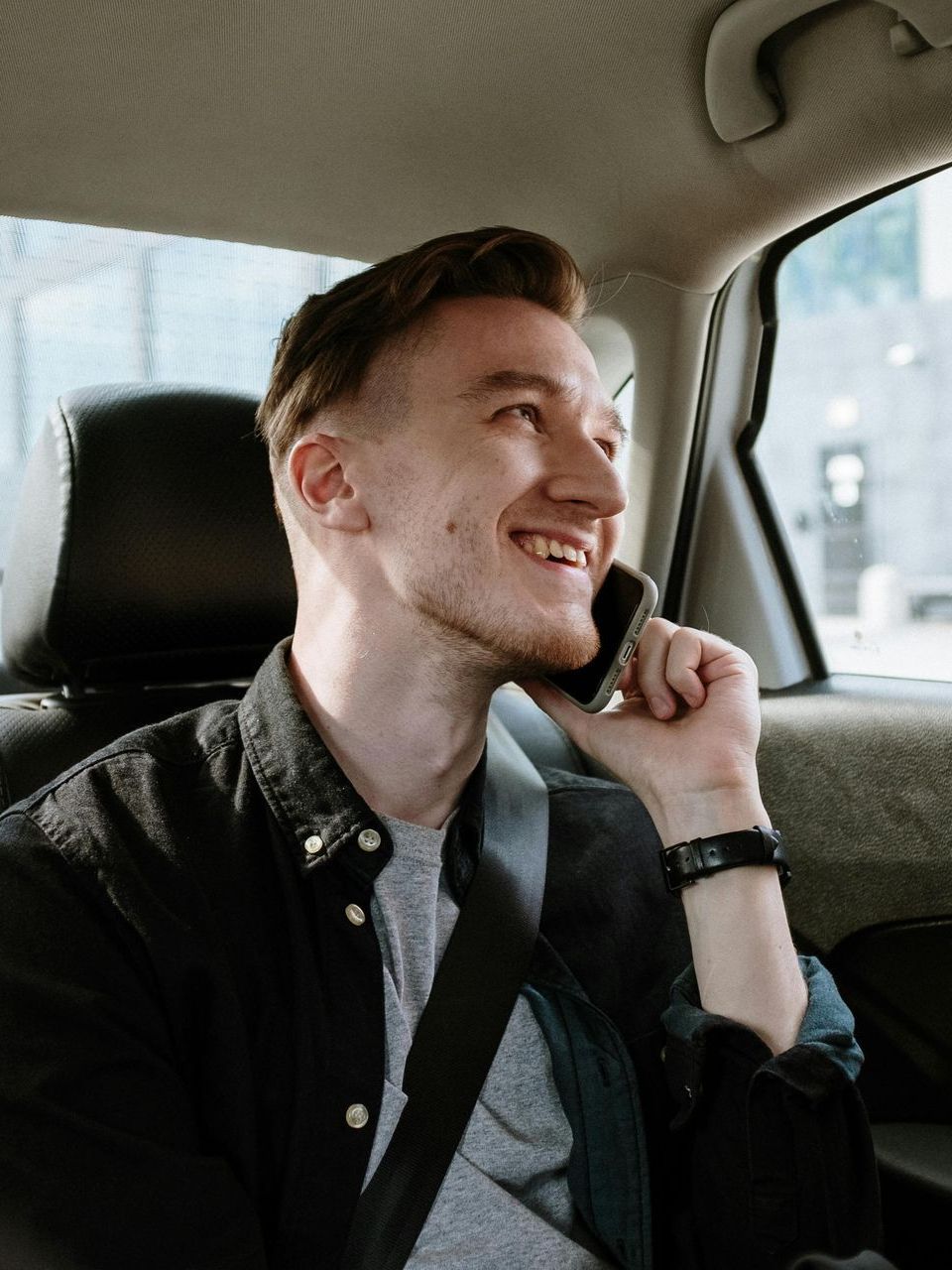 A man is sitting in the back seat of a car talking on a cell phone.