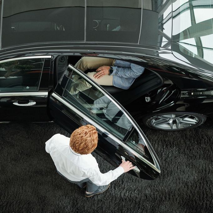 A man is opening the door of a black car in a showroom.