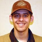 A young man wearing a hat and scarf is smiling for the camera.