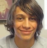 A young man with long hair is smiling in front of a picture of a man in a suit.