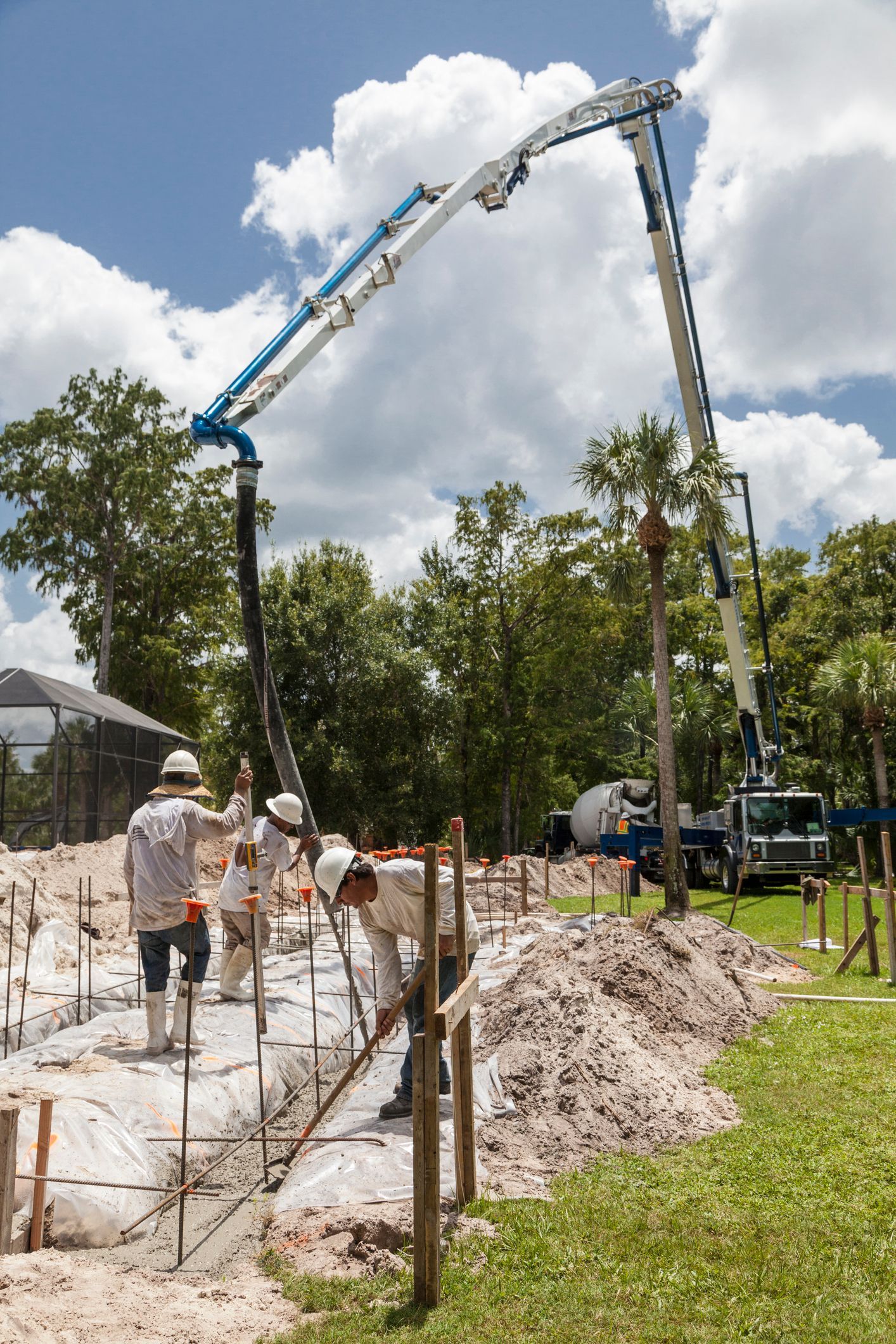 Construction crew performing residential concrete pumping at housing site with large pump hose.