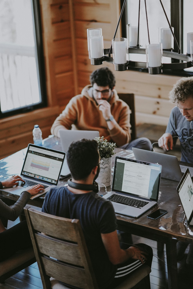 People working together at a table with laptops in a bright office.
