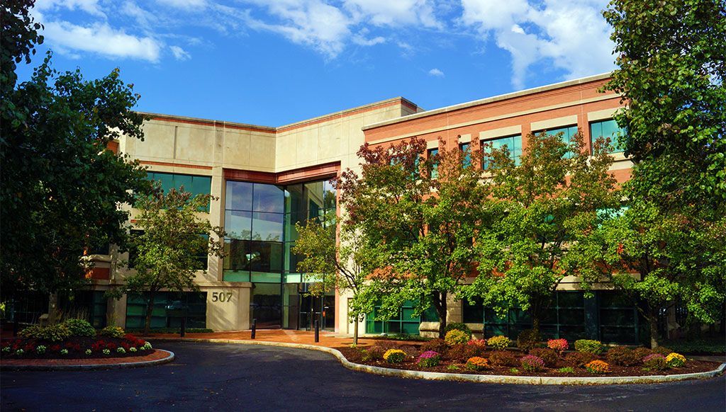 Office building with large glass windows, trees, and blue sky.