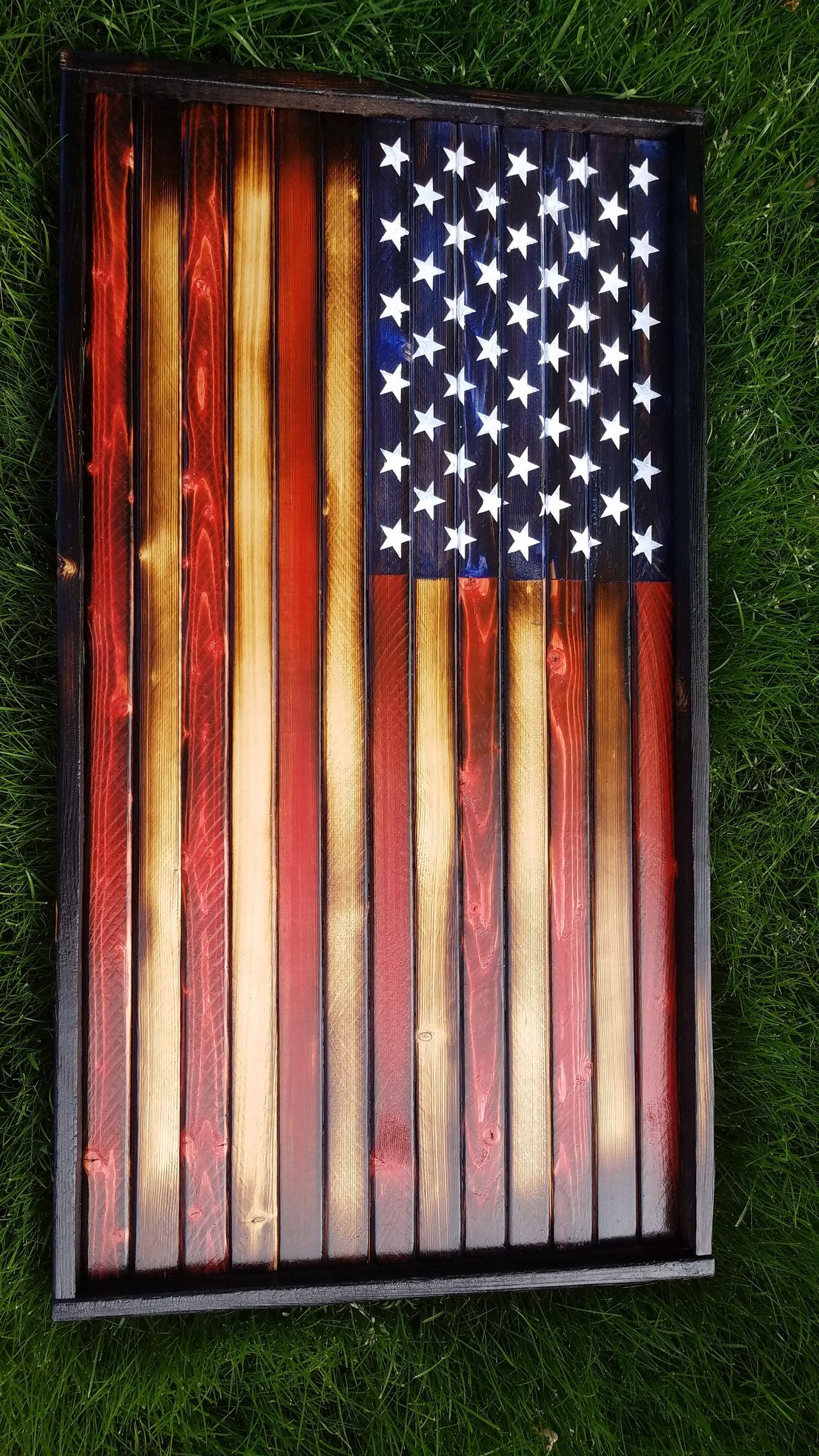 A wooden american flag is sitting on top of a lush green field.