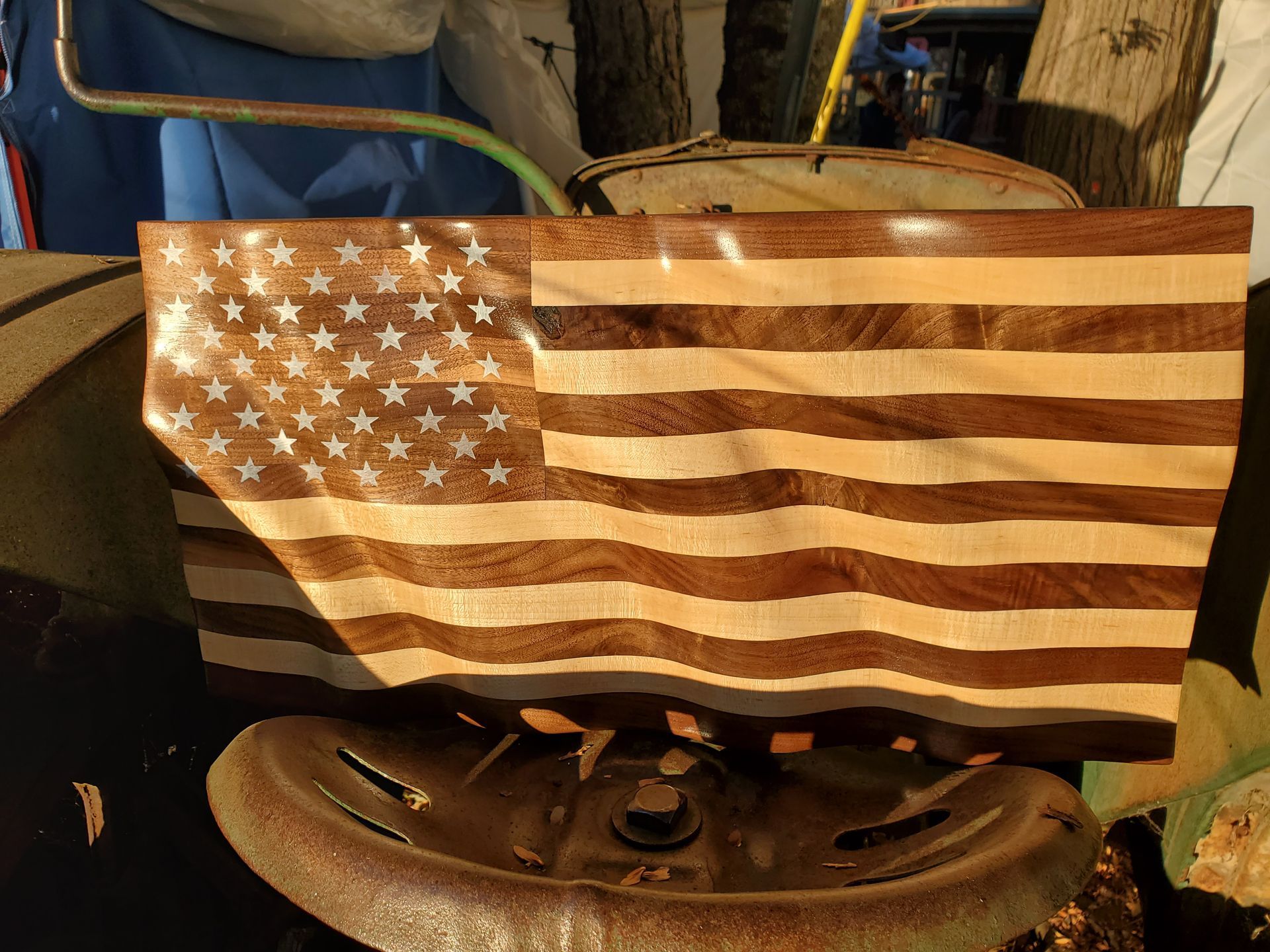 A wooden american flag is sitting on top of a rusty tractor wheel.