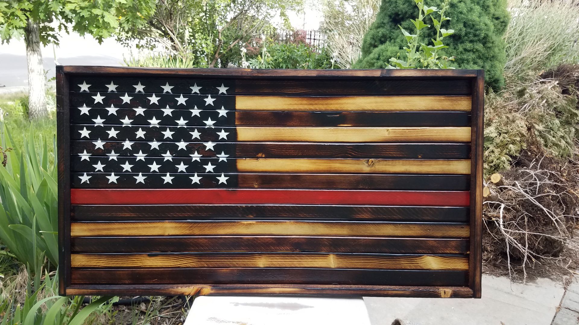 A wooden american flag with a red line in the middle is hanging on a sidewalk.