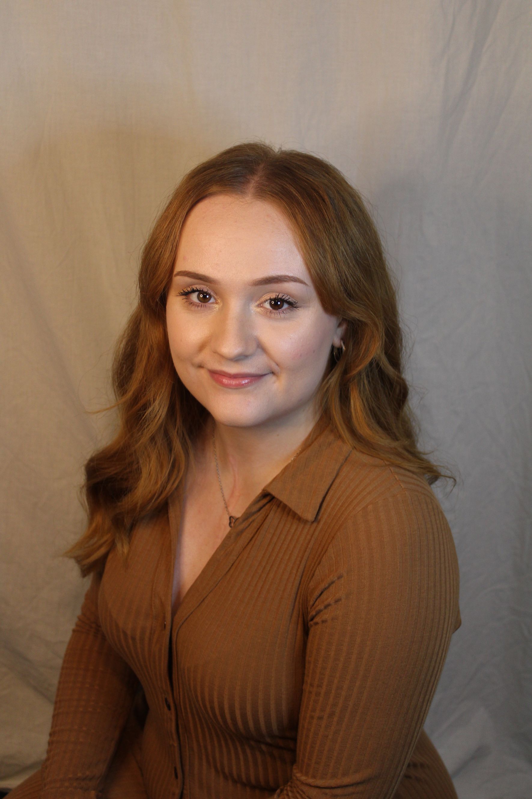 Woman with long auburn hair wearing a brown collared shirt smiles.