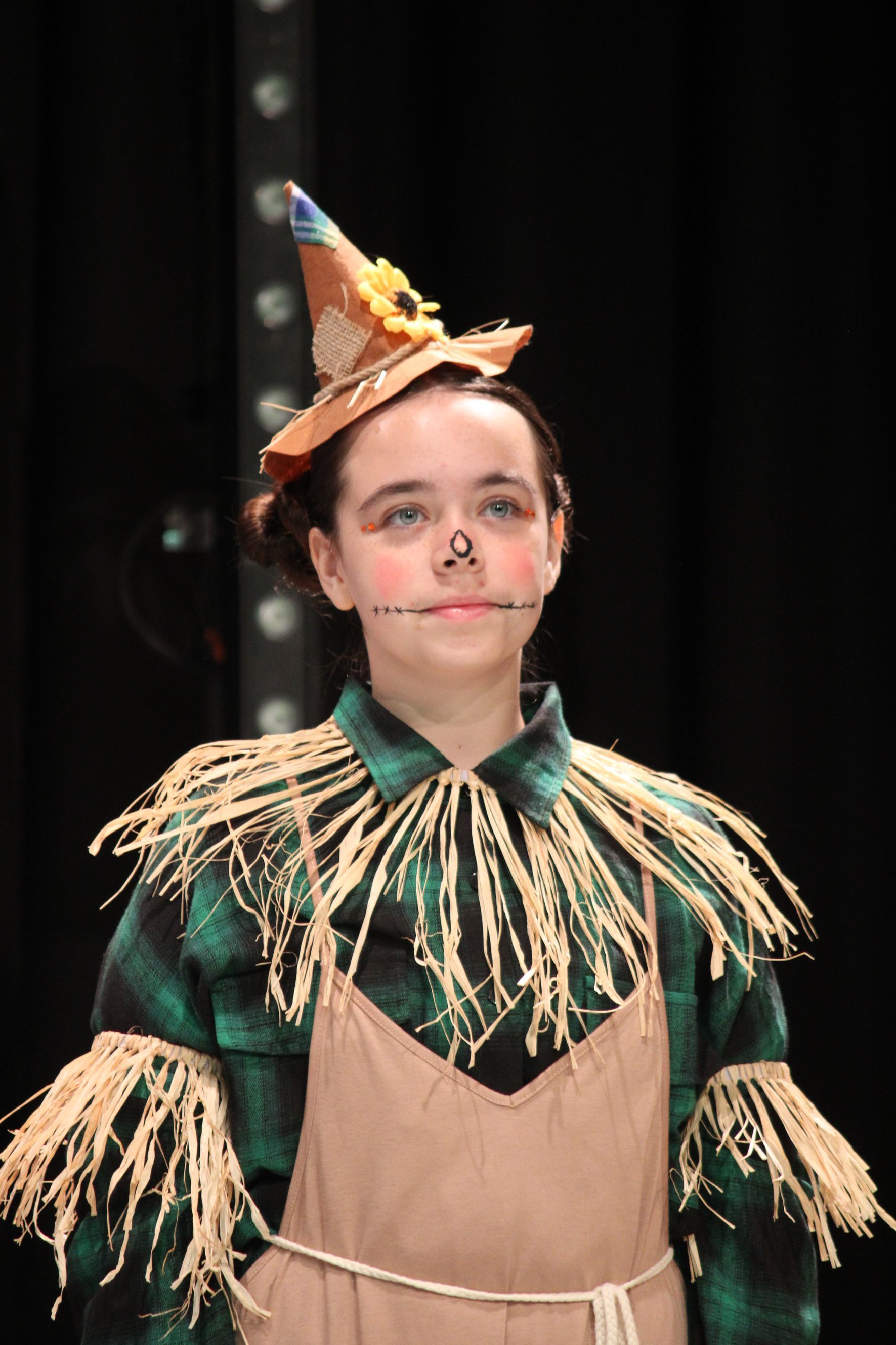 A person in a scarecrow costume, with a hat and straw details, looking up.