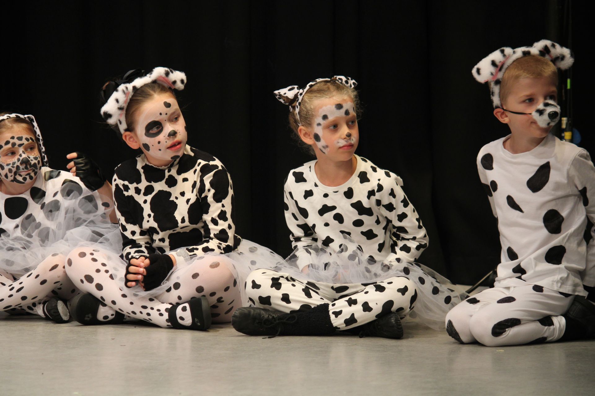 Children in Dalmatian costumes sit on a stage with black backdrop.