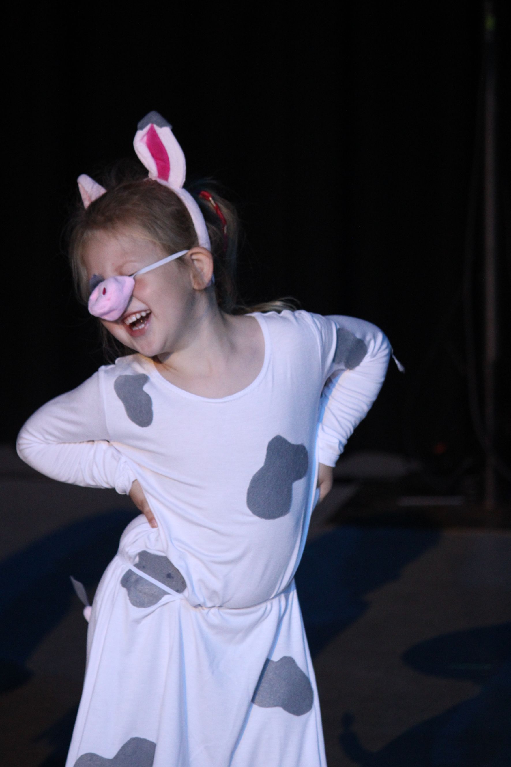 Girl in a cow costume with pink pig nose and ears. She's smiling, posing with hands on hips.