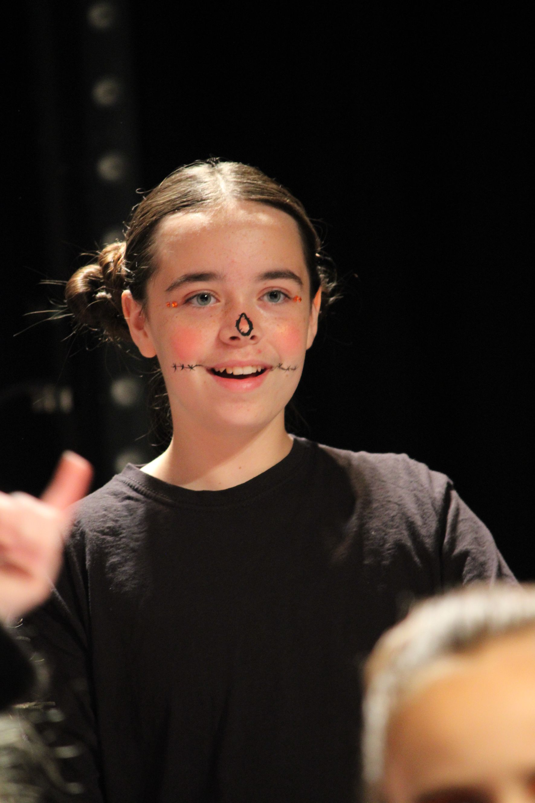 Girl with face paint and dark hair smiles against a black background.