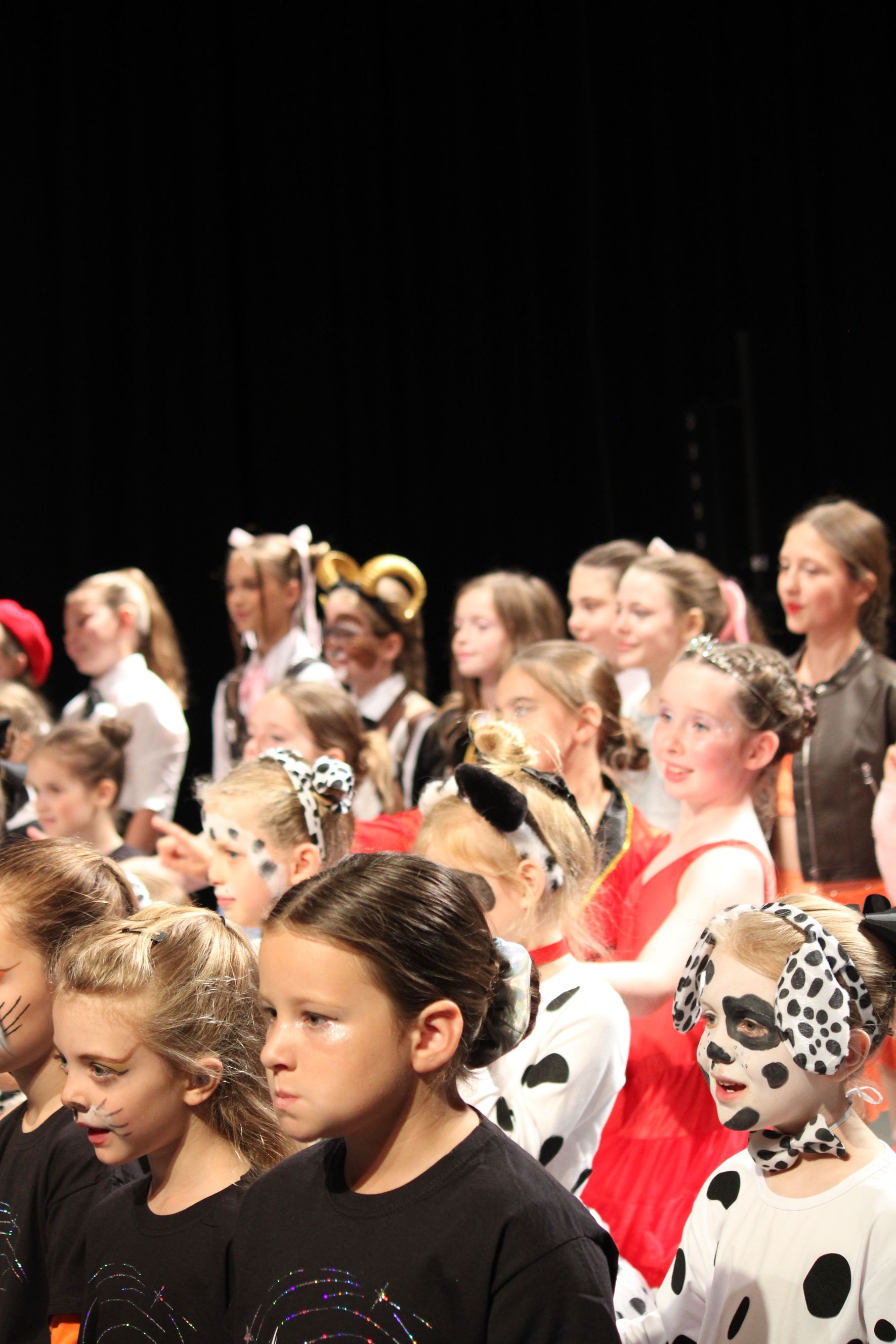 Children in Dalmatian costumes and face paint on a stage, some with props, performing.