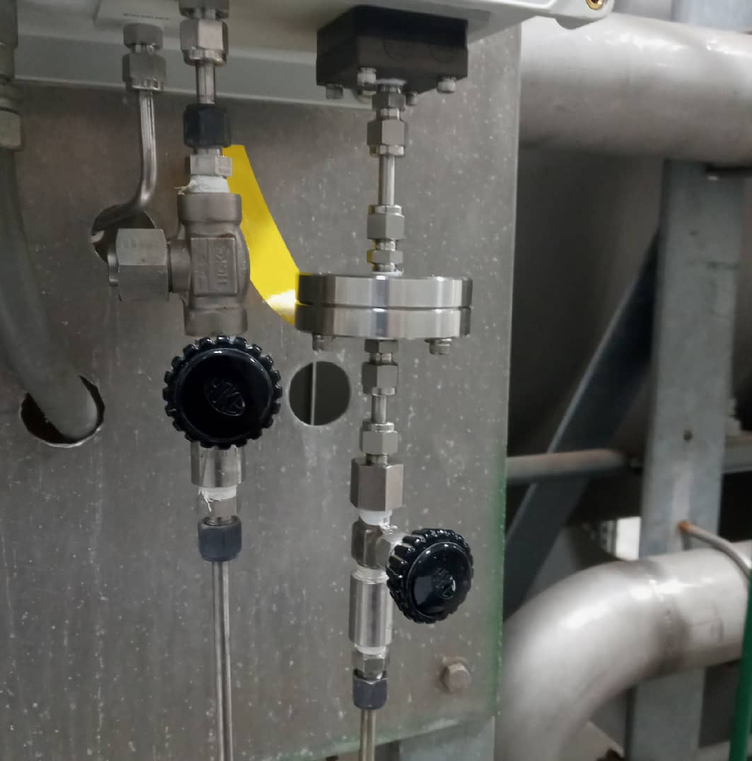 Industrial metal piping with two control valves and a circular flange unit mounted on a metal panel.