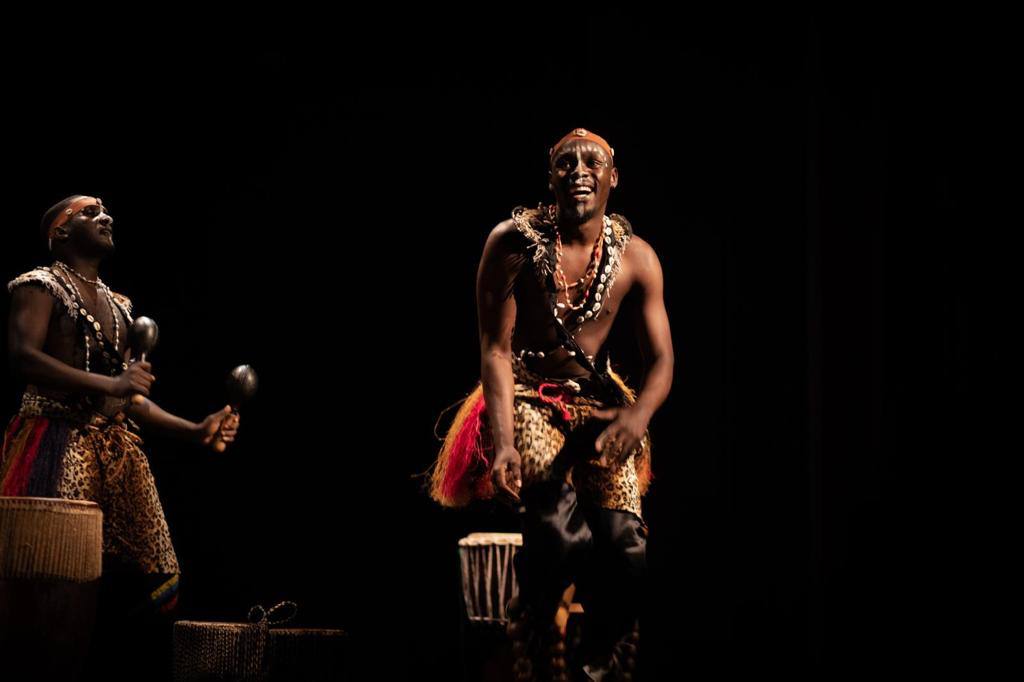 Two men are playing drums on a stage in a dark room.