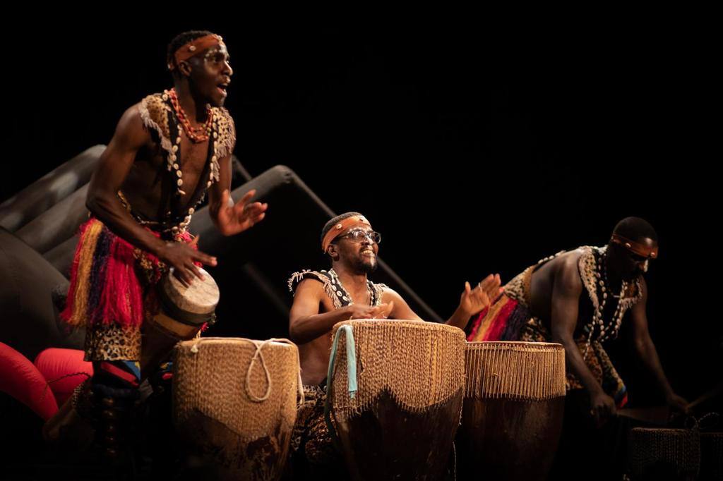 Three men are playing drums on a stage in a dark room.