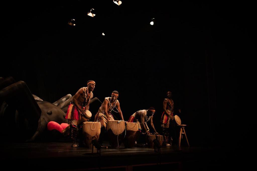 A group of people are playing drums on a stage in the dark.