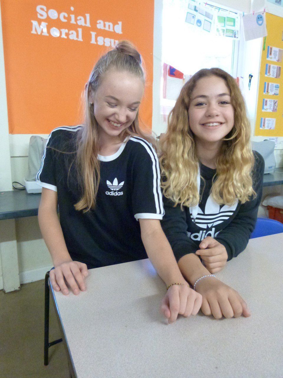 Two girls are sitting at a table in front of a sign that says social and moral issues