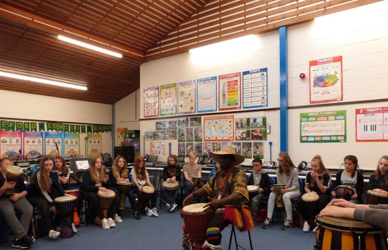 A man is playing a drum in front of a group of people in a classroom.