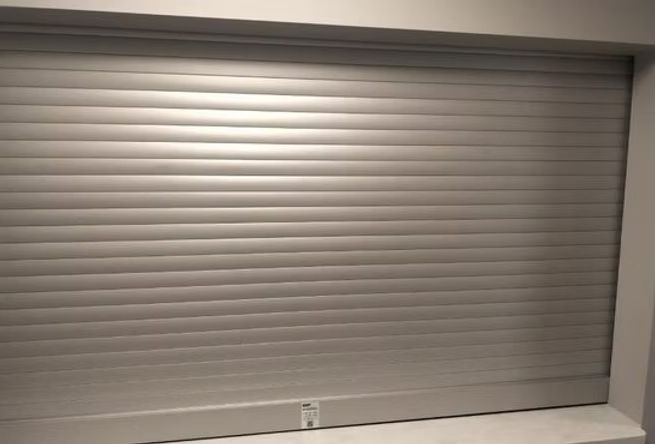 A silver roller shutter is closed on a window in a room.