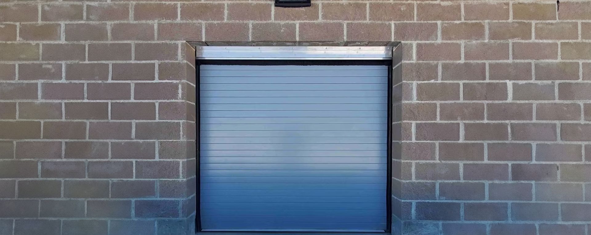 A blue garage door is sitting on a brick wall.