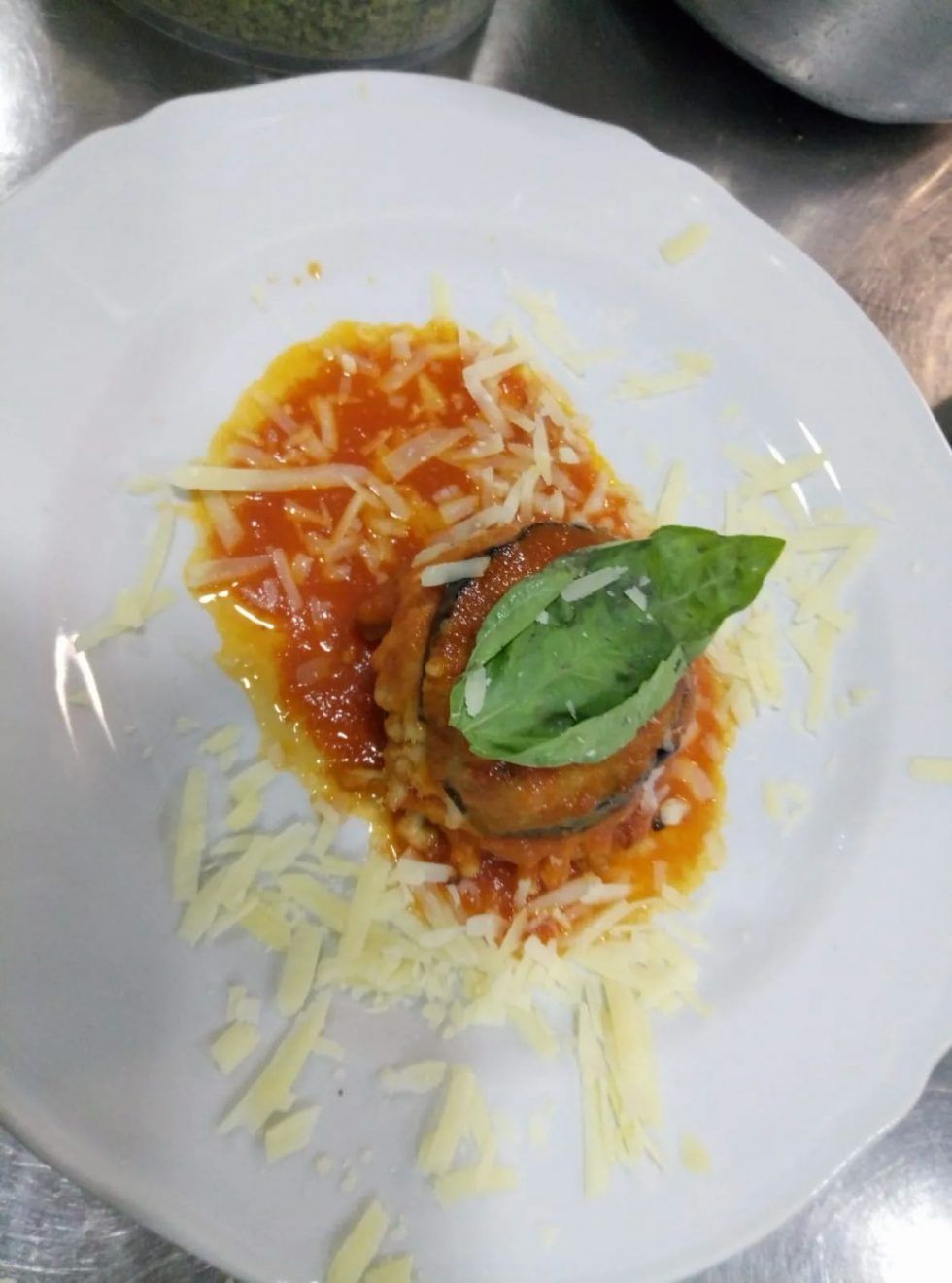 Melanzane impilate con salsa di pomodoro, formaggio e basilico su un piatto bianco.
